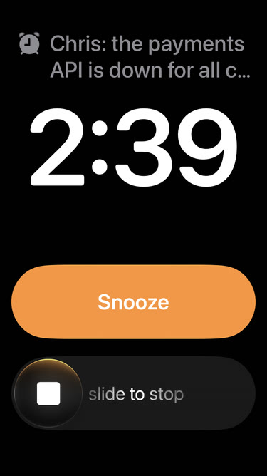 A Clock alarm ringing on the Lock Screen. The label reads: Chris: the payments API is down for all c… followed by the time 2:39, a Snooze button and slide to stop.